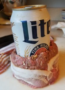 Forming the burger around the beer can and wrapping it with bacon.